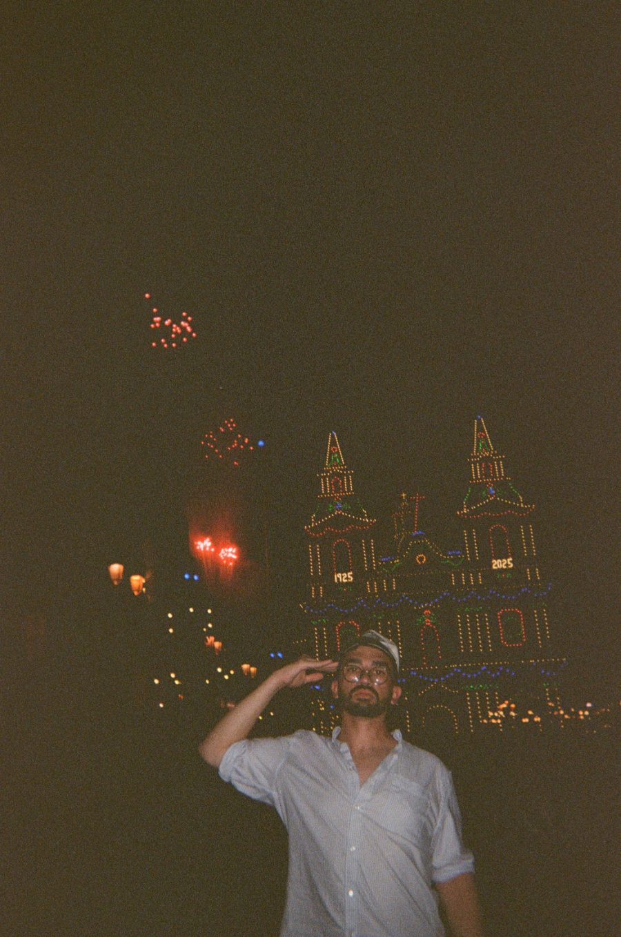Zack Fenech saluting in front of an illuminated church at night, with fireworks in the sky
